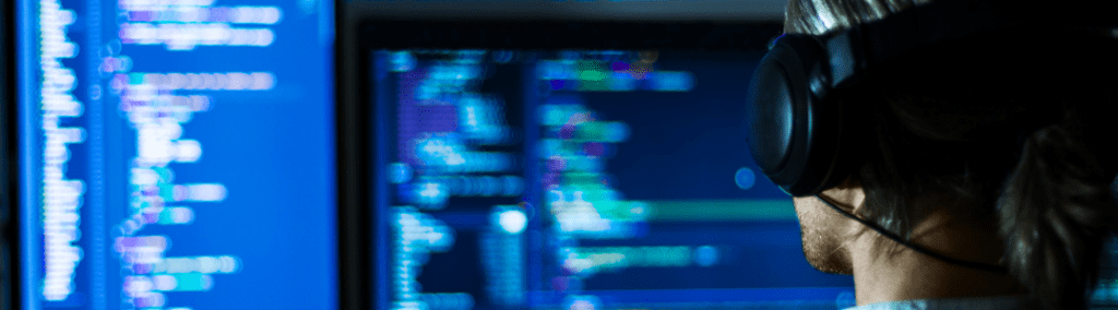 Man with headphones in front of a large monitor with code on it