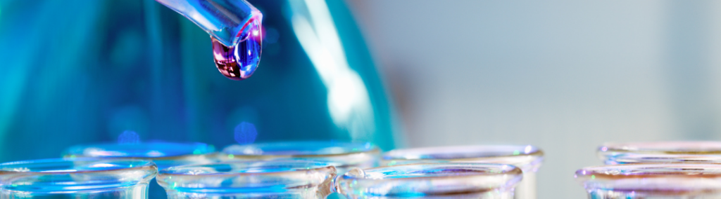 Close up of liquid in a dropper above test tubes